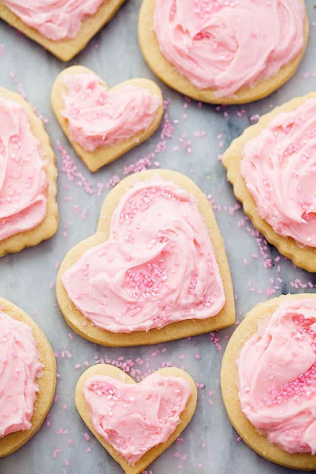 You cannot beat homemade sugar cookies with a crisp edge and a soft center. These are the BEST! Topped with my favorite cream cheese frosting and sprinkles, these sugar cookies are a tried and true favorite. Froster sugar cookies on a baking sheet lined with parchment paper.