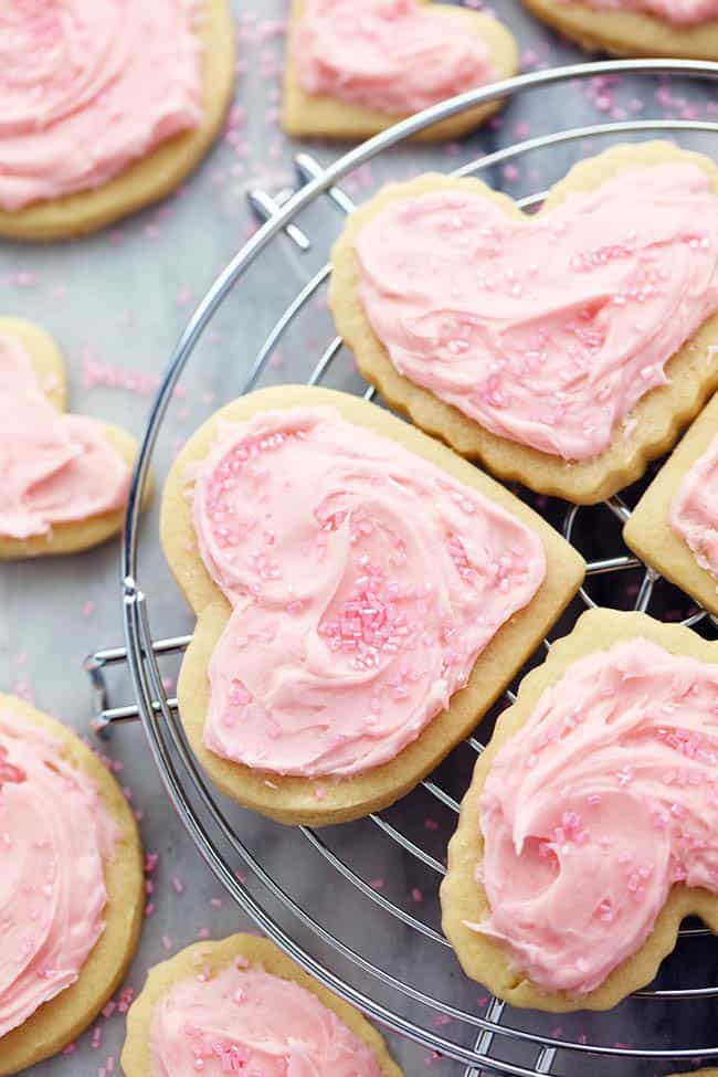 You cannot beat homemade sugar cookies with a crisp edge and a soft center. These are the BEST! Topped with my favorite cream cheese frosting and sprinkles, these sugar cookies are a tried and true favorite. Frosted sugar cookies with sprinkles on a cooling rack.