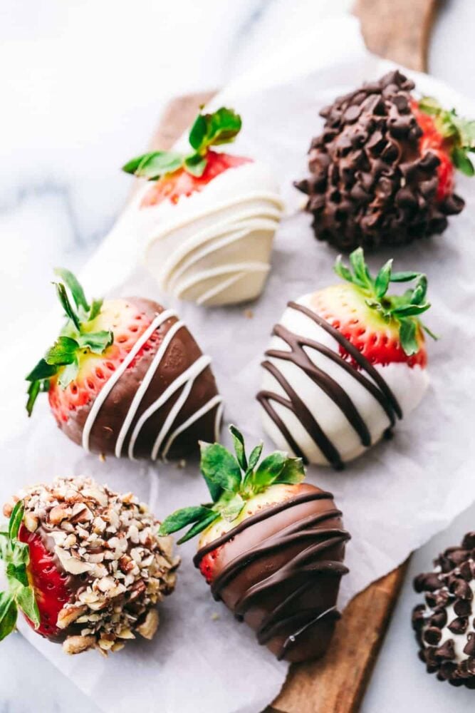 Chocolate Covered Strawberries are a simple dessert that takes a ripe, juicy strawberry dipped in meltedย chocolate andย drizzled or dipped in various toppings to make a sweet treat. Melt someones heartย with this decadent dessert!ย Chocolate covered strawberries on a cutting board.