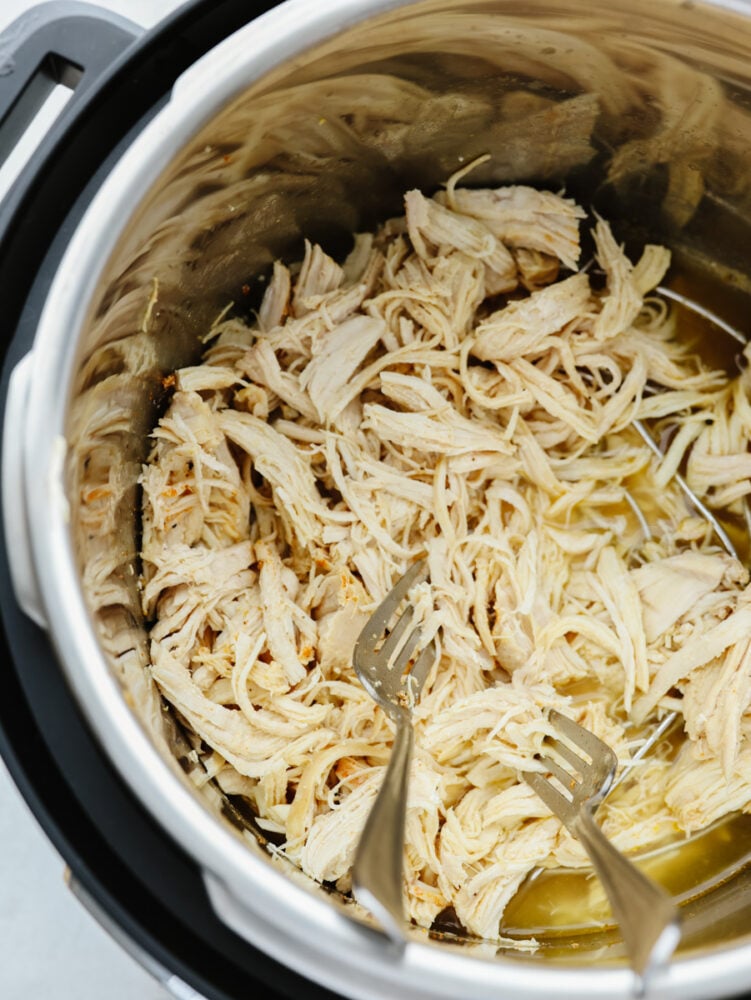 This instant pot shredded chicken is the solution to all of your chicken needs! It's seasoned, moist, and easy to shred, which makes it the perfect go-to recipe when you need shredded chicken for any dish. Chicken being shredded with two forks in and instant pot.