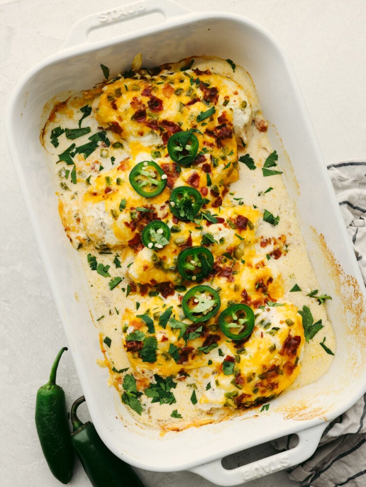 Dinnertime-ready, this jalapeno popper chicken is creamy and delicious with the perfect amount of heat! It has all of the flavors of your favorite appetizers, but in one easy-to-make meal! Jalapeno popper chicken in a white casserole dish, garnished with cilantro.