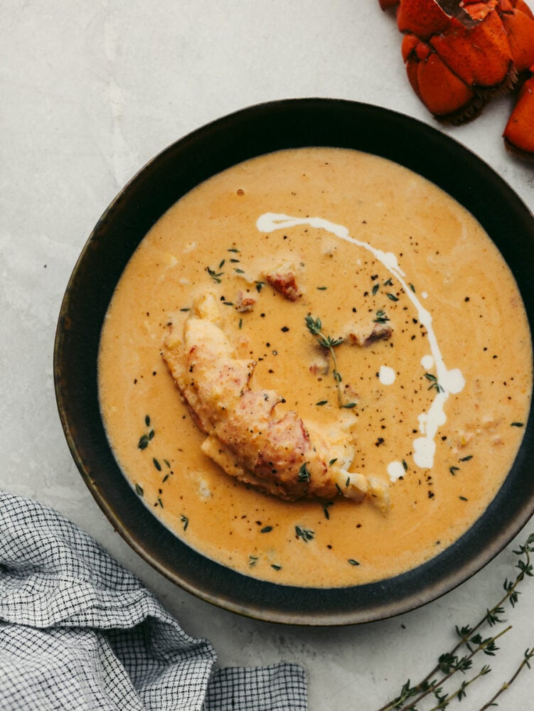 Classy, elegant, and insanely delicious, this lobster bisque needs to make its way to your dinner menu as soon as possible! This recipe is absolutely divine and not one you will want to miss out on! A bowl of lobster bisque with garnish and a lobster tail in it.