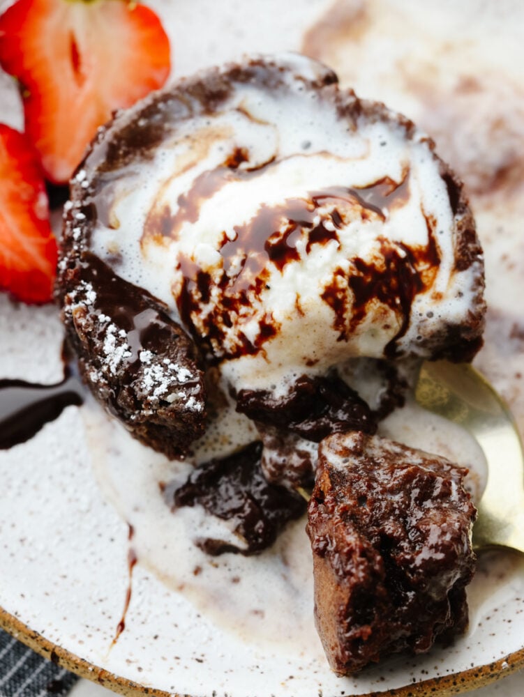 Chocolate lava cake is the ultimate dessert. It's a showstopper, moist cake that has an oozing chocolate center. Your guests will go crazy over this recipe! A close up of chocolate lava cake with melting ice cream and a spoon cutting into it.