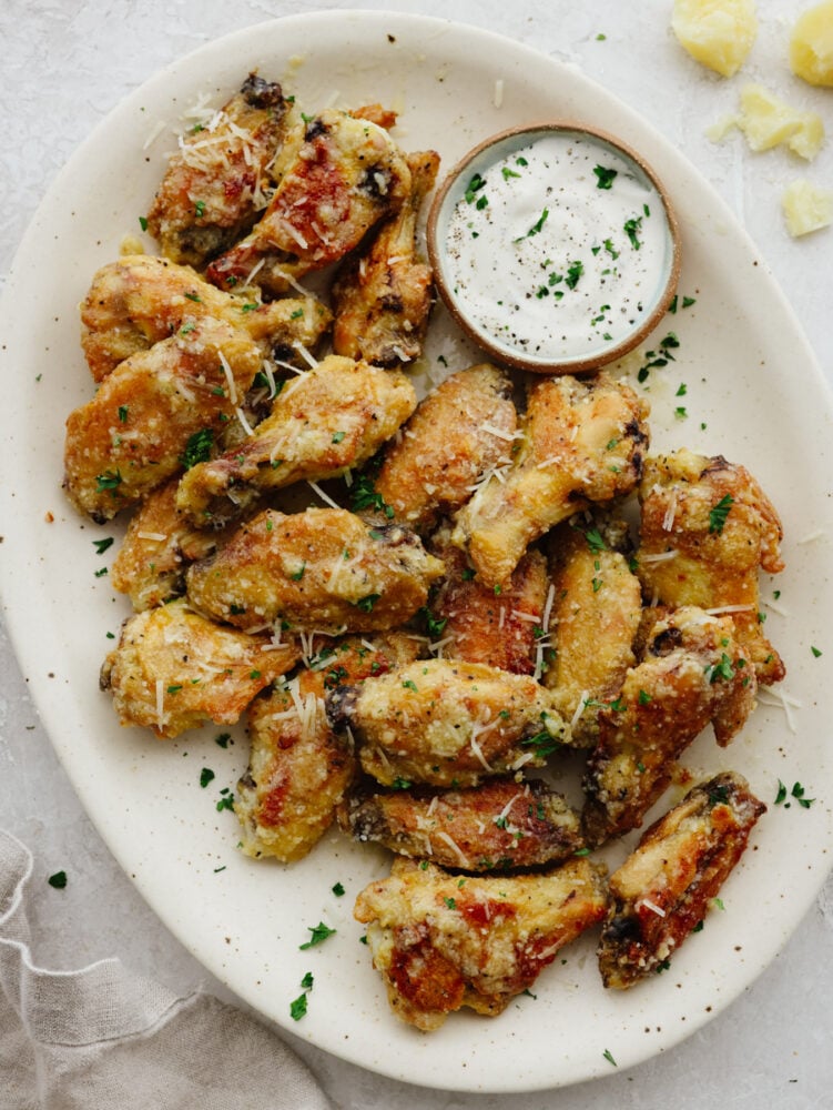 If you love wings, then these parmesan garlic ones are going to blow you away! The parmesan, honey, and garlic sauce are so delicious that these wings are going to fly off of your table! A platter of winger with ranch dipping sauce.