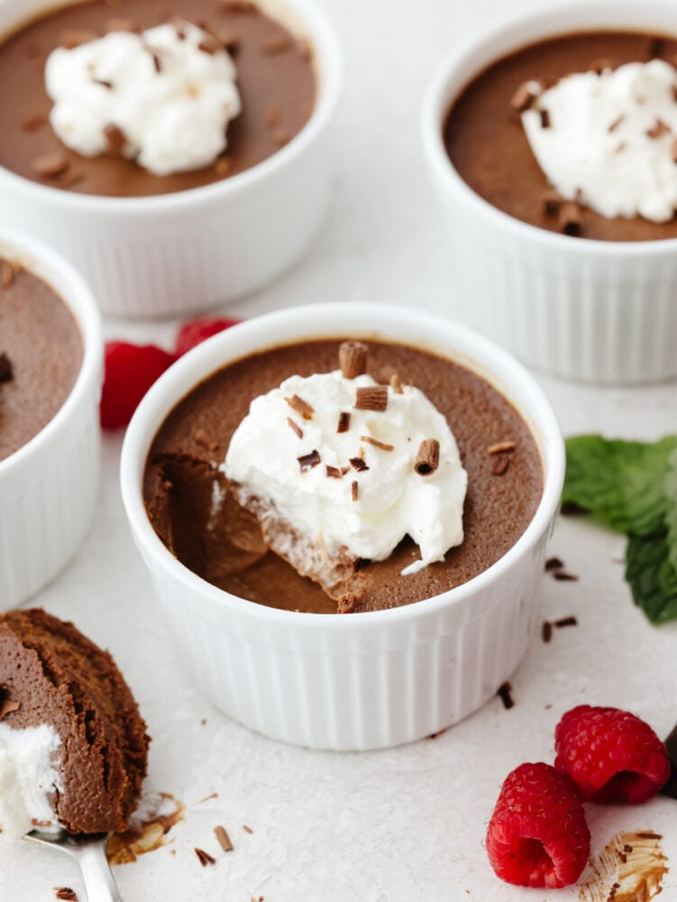 Pot de crème is silky smooth and loaded with chocolate flavor. Perfectly proportioned in individual servings, you can end any meal on a high note with this delectable dessert! Pot de creme with whipped cream and chocolate shavings on top with a scoop taken out of the ramekin.