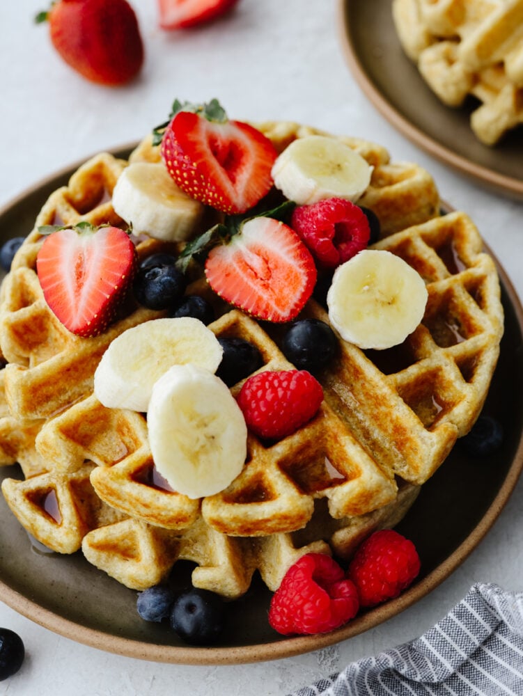 Get ready for some delicious and healthy waffles that are going to knock your socks off! These protein waffles are absolutely delicious, and you can whip them up in less than 10 minutes! Waffles on a plate topped with bananas, blueberries, strawberries or raspberries.
