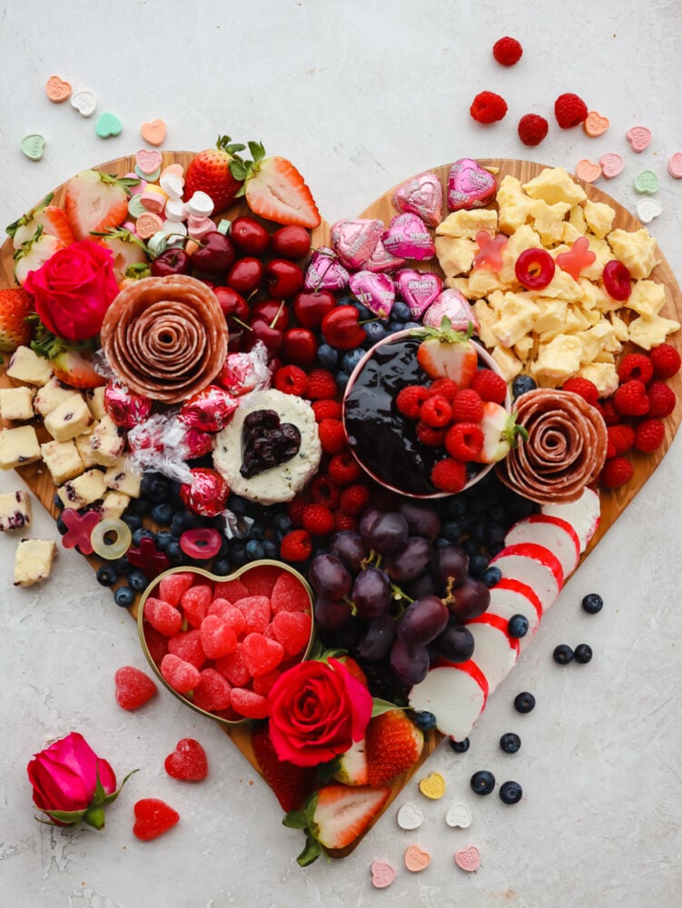 The holiday of love is just around the corner, and you need to try out this Valentine's day charcuterie board! It's packed with meat, cheeses and all sorts of festive red and pink fruits and candy to start the holiday off right. Meats, cheese, fruit and candy on a heart shaped wood cutting board.
