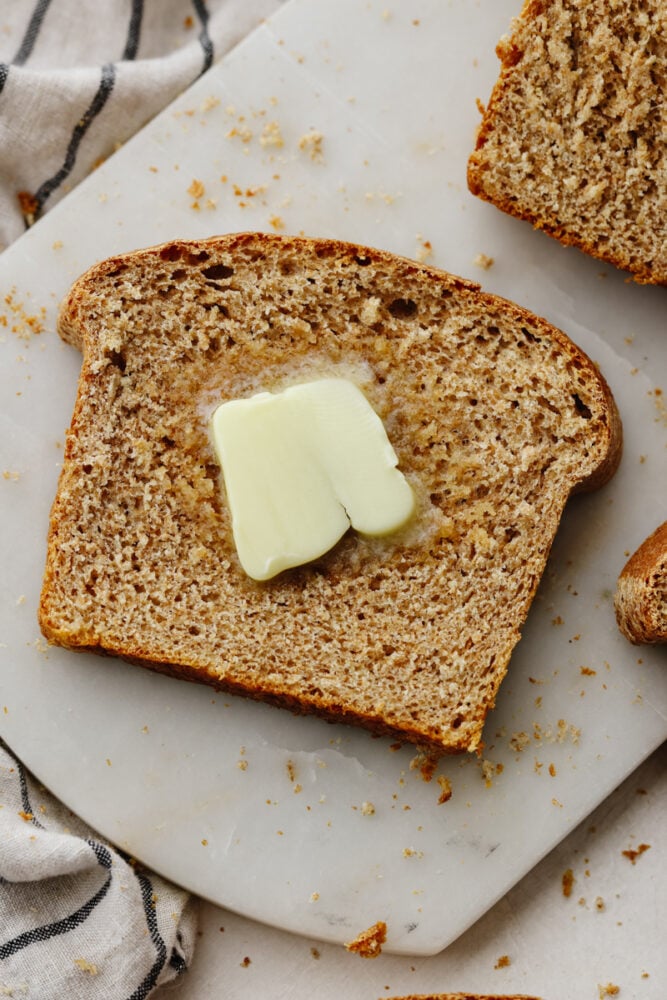 One slice of this amazing wheat bread and you'll be addicted! It's warm, soft, and tender, sweetened to perfection with honey! A slice of bread with butter on it.