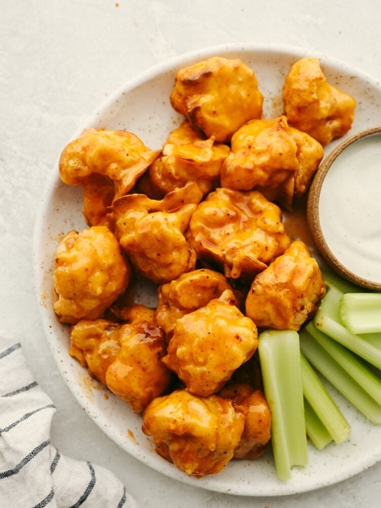 This low-carb take on wings is going to rock your world! Draped in a sticky-sweet honey buffalo sauce, these easy air fryer cauliflower wings are absolutely to die for! Air fryer honey buffalo cauliflower wings served on a white stoneware plate alongside ranch and celery.