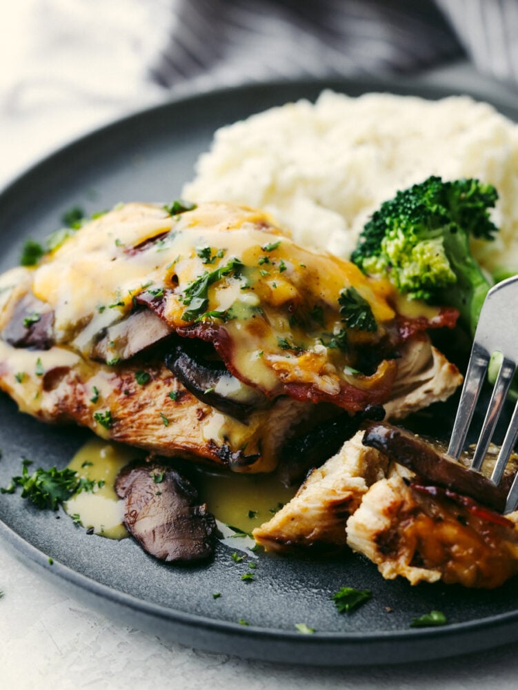 This copycat Alice Springs Chicken is a zesty, cheesy dinner that the whole family will enjoy! It's super easy to make and loaded with toppings like honey mustard, bacon, and colby jack cheese! Alice Springs Chicken served on a gray plate with broccoli and mashed potatoes.