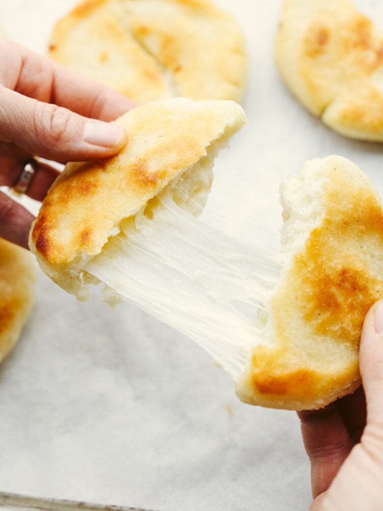 Arepas are a delicious cheesy bread made out of cornmeal! This super simple Colombian treat is sure to win the hearts of your family. Holding an arepa that has been torn into 2 pieces.