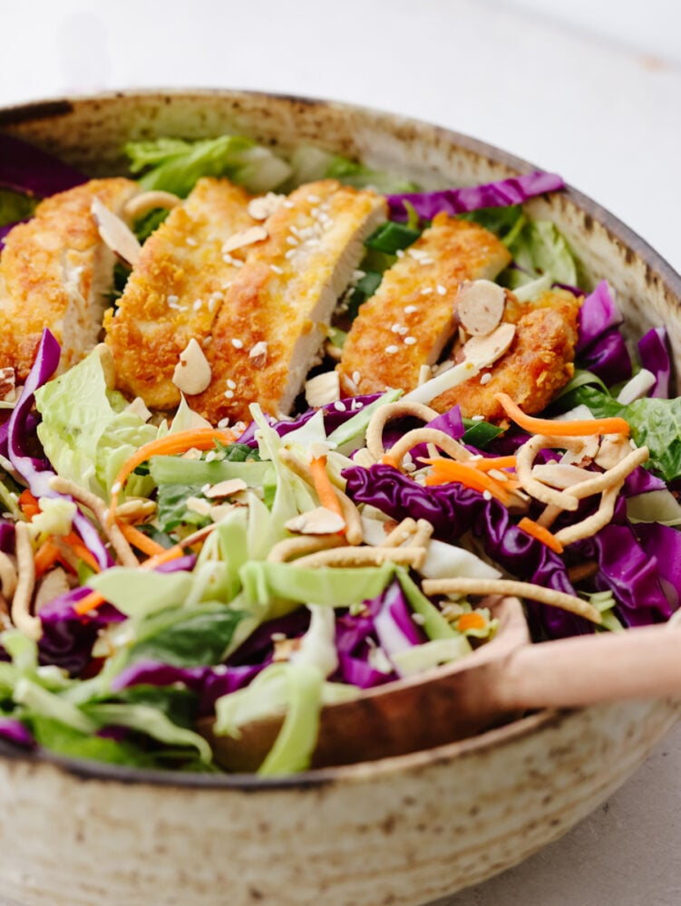This Asian chicken salad is packed with crispy greens, crunchy chicken, toasted almonds, and chow mein noodles. It's tossed with a light and delicious creamy vinaigrette and will be your new go-to salad! A close up of Asian chicken salad being mixed with a wooden spoon.