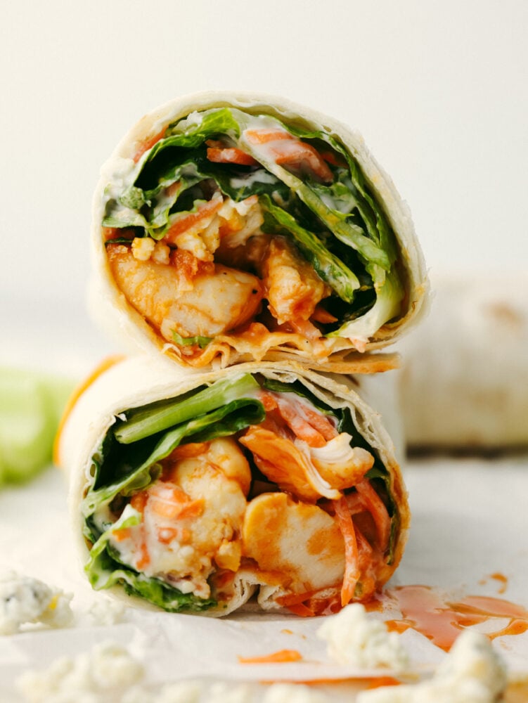 These honey buffalo chicken wraps are so healthy and delicious! They're loaded with a sweet buffalo sauce, ranch, bleu cheese, and all of your favorite veggies for a lunch you'll love! Two buffalo chicken wraps stacked on top of each other.