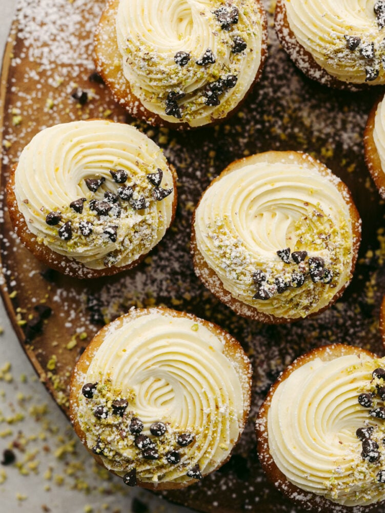 All the cannoli flavors you love in a bite-sized cupcake! Cannoli cupcakes are moist and tender with the most delicious mascarpone whipped cream frosting! Top-down shot of cannoli cupcakes on a wooden board.