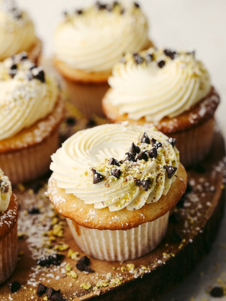 All the cannoli flavors you love in a bite-sized cupcake! Cannoli cupcakes are moist and tender with the most delicious mascarpone whipped cream frosting! Closeup of a cupcake topped with mascarpone frosting, chocolate chips, and pistachio pieces.