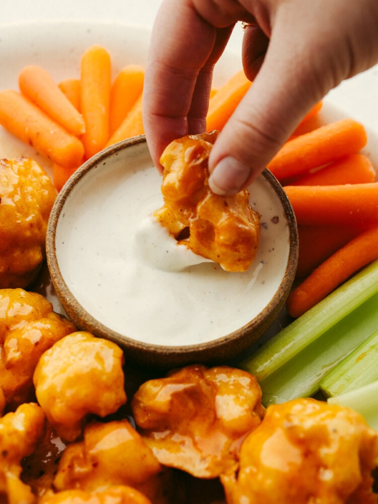 This healthier take on wings is insanely delicious! Coated in a delicious honey buffalo sauce, these cauliflower wings are so good that you will forget that you are even eating a vegetable! Cauliflower wings on a platter with one being dipped into ranch sauce.