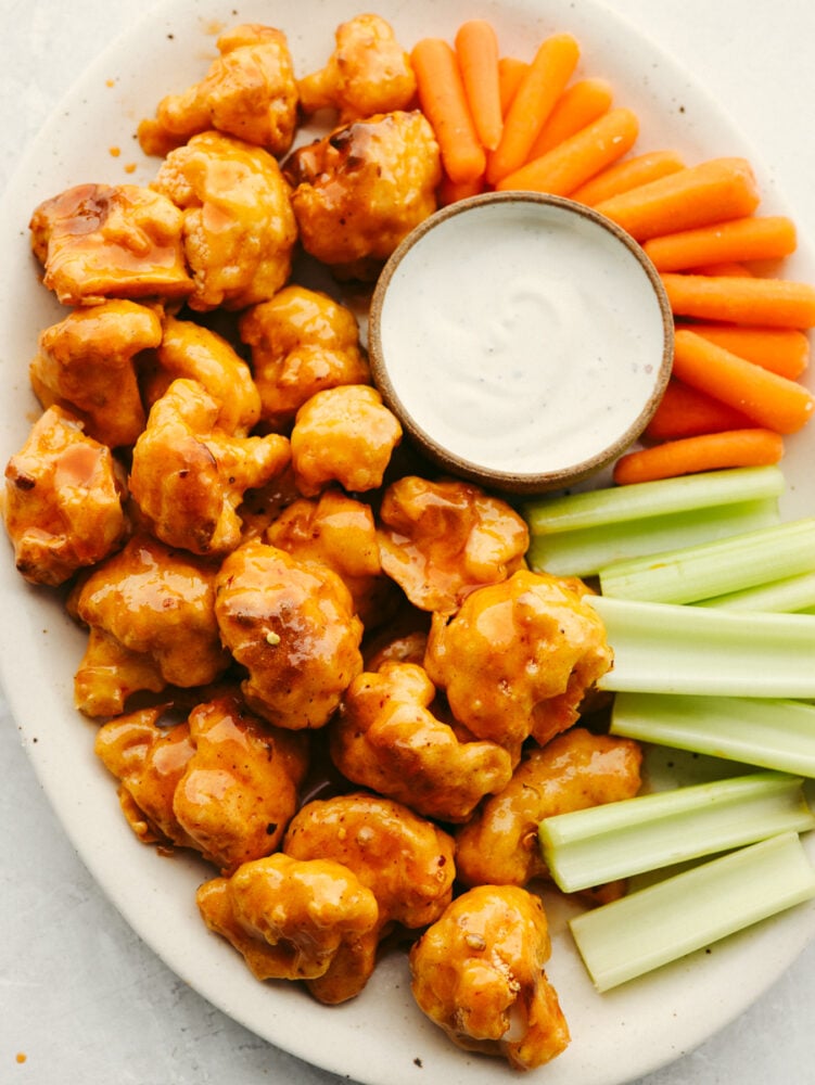 This healthier take on wings is insanely delicious! Coated in a delicious honey buffalo sauce, these cauliflower wings are so good that you will forget that you are even eating a vegetable! A platter with cauliflower wings, celery, carrots and some ranch dressing.