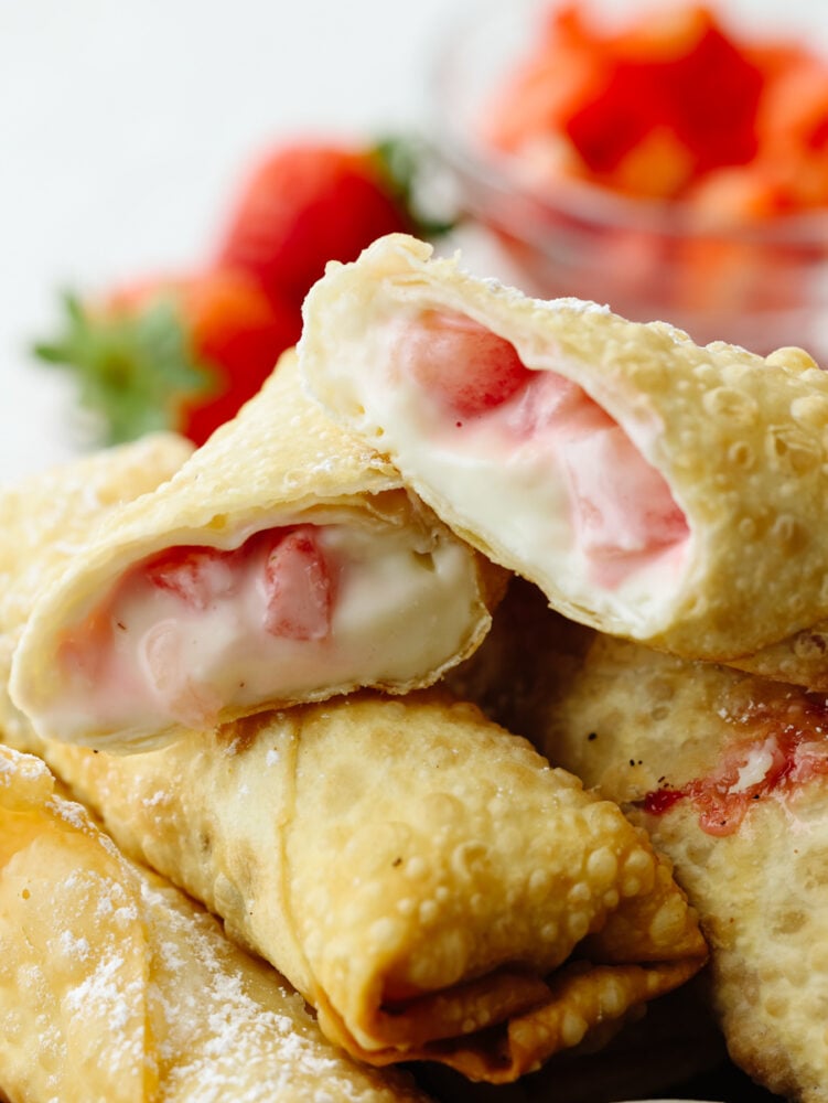Crispy on the outside with a creamy, strawberry filling on the inside, these cheesecake egg rolls are the BEST. Your guests will eat one and won't be able to stop! A zoomed in picture of a cheesecake egg roll that is cut in half.