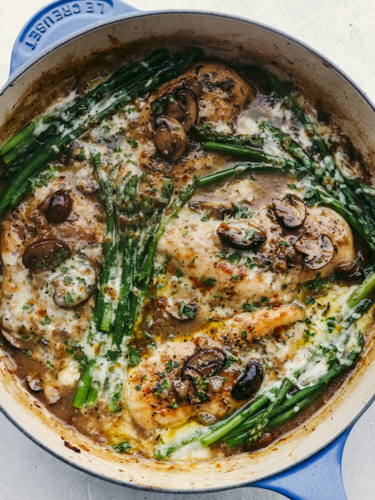 Juicy chicken is covered in creamy Madeira sauce, melty cheese, mushrooms, and asparagus in this easy skillet recipe! Chicken Madeira brings all of those delicious Cheesecake Factory flavors right to your kitchen! Chicken with mushrooms, cheese, and asparagus in a skillet.