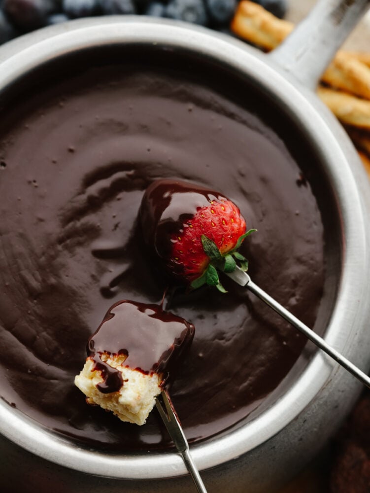 The best way to impress your valentine is with homemade chocolate fondue! This silky-smooth dessert is so amazing and pairs perfectly with all of your favorite treats! Closeup of a strawberry and marshmallow being dipped in chocolate fondue.