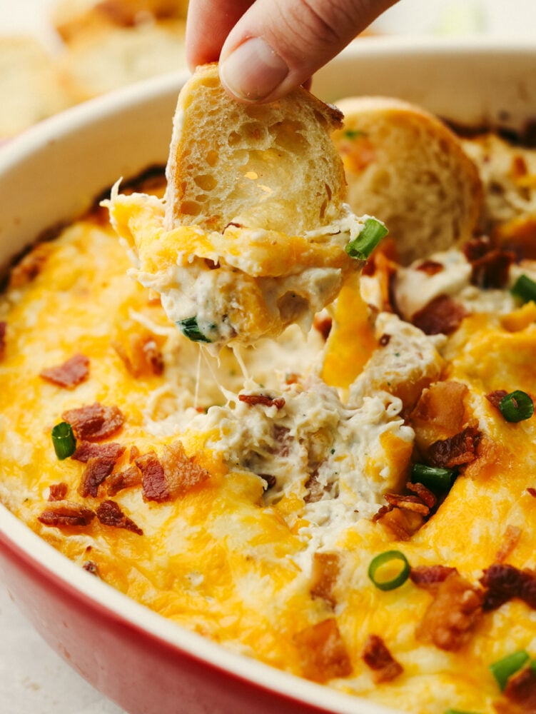 You won't find a better dip out there than this crack chicken dip! It's cheesy and packed with chicken, and bacon and seasoned to perfection. It will be the best appetizer dip that you've ever had! A close up of crack chicken dip with a small piece of bread being dipped into it.