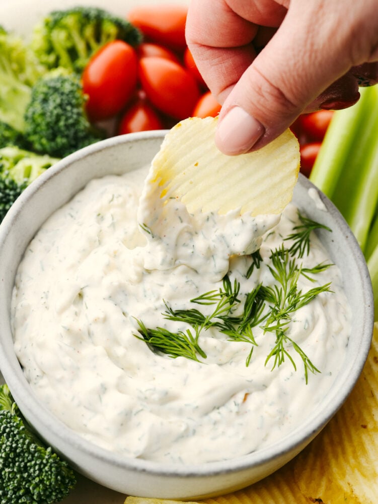 This delicious dill dip is easy and goes with everything. It is creamy and full of flavor and will be ready to eat in less than 5 minutes! If you are a dill pickle lover like me then you are going to be bringing this to every party and get-together! A potato chip being dipped into dill dip.