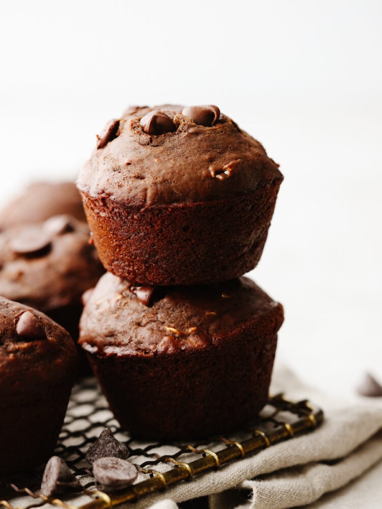 These double chocolate muffins are a healthier choice than some others you may find out there! They are still packed with delicious ingredients, and the chocolate flavor will blow you away. A stack of double chocolate muffins on a baking sheet.