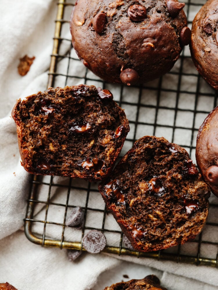 These double chocolate muffins are a healthier choice than some others you may find out there! They are still packed with delicious ingredients, and the chocolate flavor will blow you away. A muffin cut in half on a cooling rack.