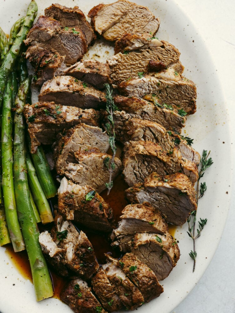 This juicy Instant Pot pork tenderloin is the perfect choice for dinner! It cooks up in 15 minutes and is full of so much flavor! Sliced tenderloin on a white plate served with asparagus.