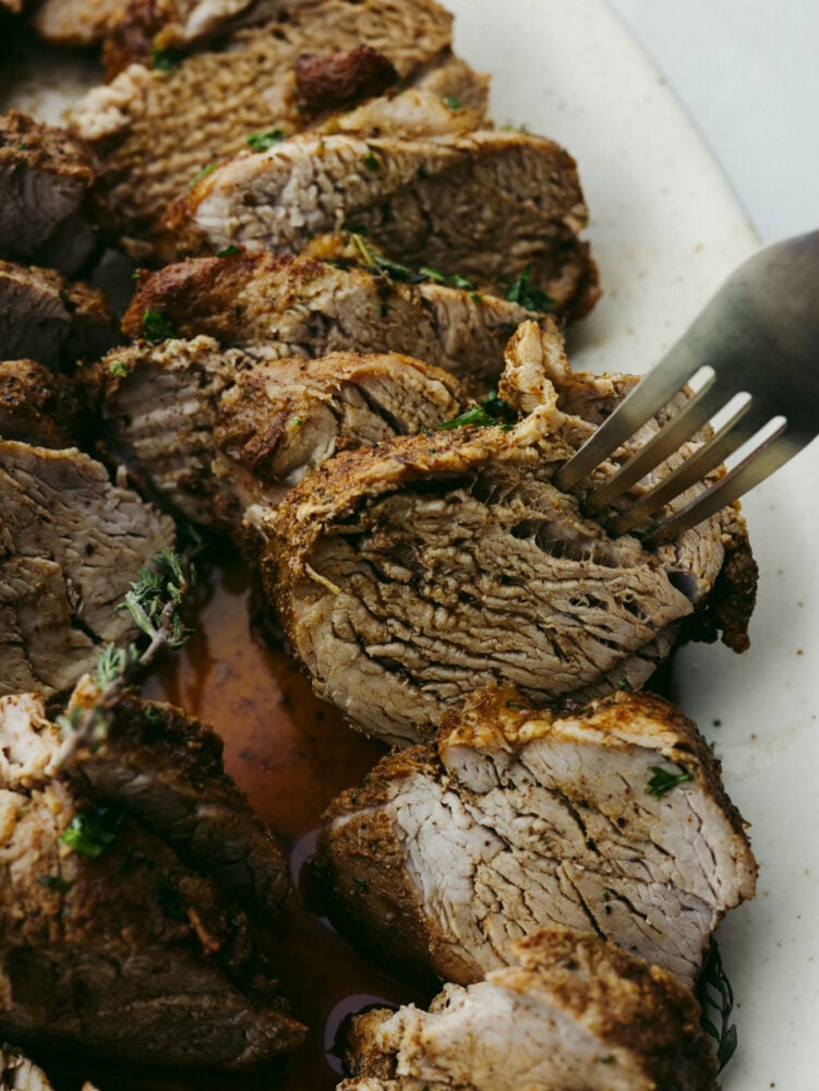 This juicy Instant Pot pork tenderloin is the perfect choice for dinner! It cooks up in 15 minutes and is full of so much flavor! Closeup of taking a slice of tenderloin with a fork.