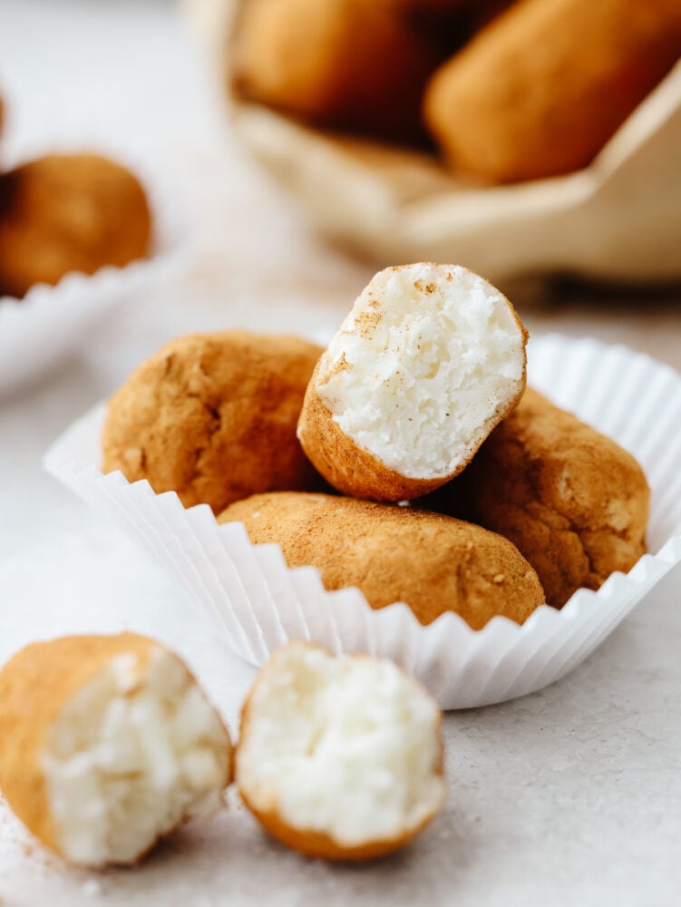 Irish potato candy is a no-bake treat filled with cream cheese and coconut flakes and then topped with cinnamon. These aren't your regular potatoes, they are candy, and I am here for it! Irish potato candy in a cupcake wrapper. Some broken in half to show the inside of the candy.
