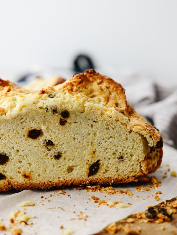 This traditional no yeast bread recipe is a crumbly dense bread with a slightly sweet taste. With only a few pantry and refrigerator staples required, this delicious traditionalย soda bread can be made easily and is one everyone will enjoy. A close up side view of a load of soda bread.
