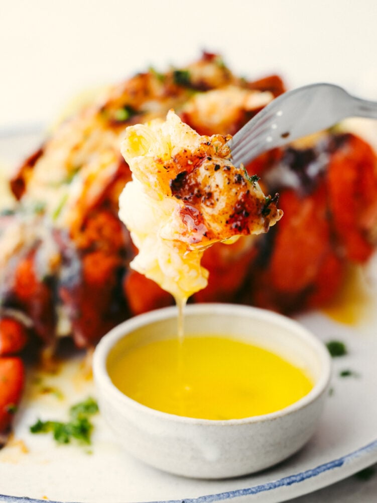 These lobster tails cooked in the air fryer are incredibly tender and delicious. Topped with a melted buttery garlic herb sauce, this is a quick and easy way to have that delectable fancy dinner without a lot of time and preparation! Lobster being dipped in butter using a fork.