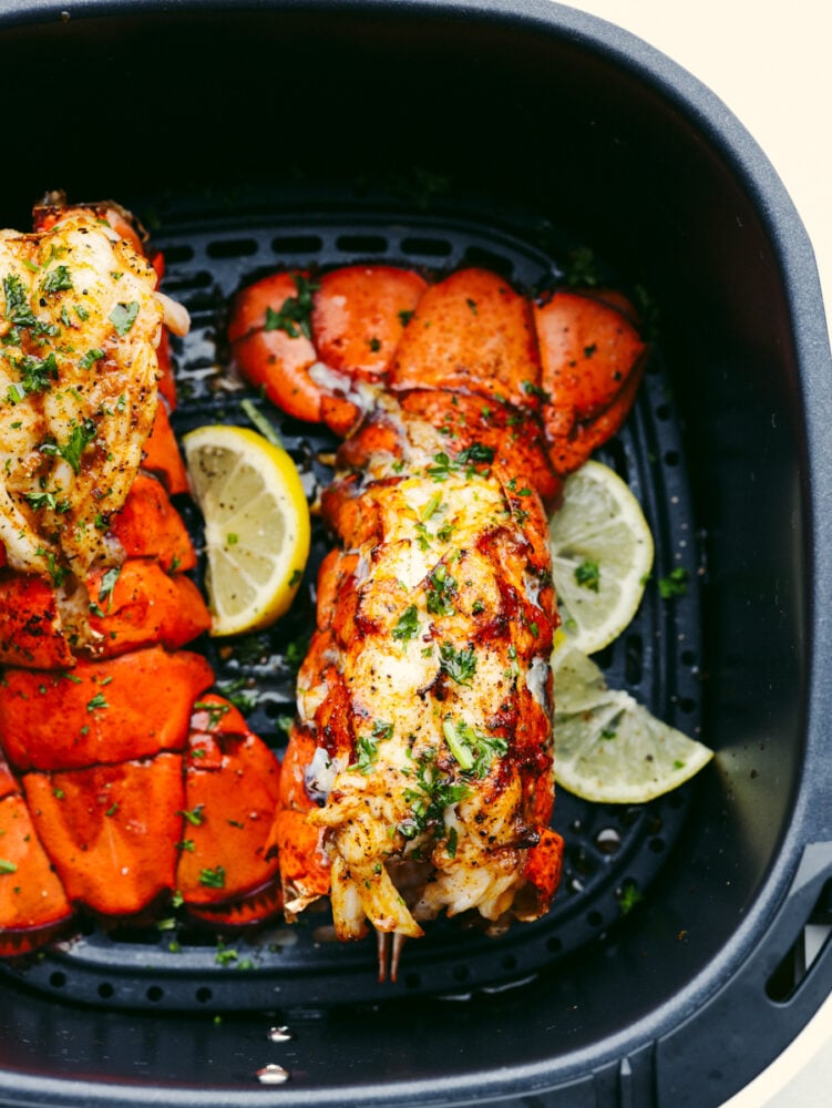 These lobster tails cooked in the air fryer are incredibly tender and delicious. Topped with a melted buttery garlic herb sauce, this is a quick and easy way to have that delectable fancy dinner without a lot of time and preparation! Lobster tails in the air fryer with lemon slices.