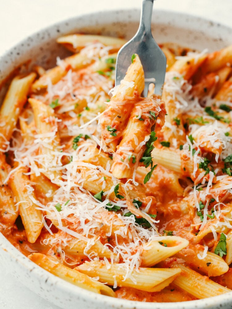 Level up pasta night with this irresistible roasted red pepper sauce! It's creamy, cheesy, and delicious with smoky, sweet spice. Be sure to make enough for seconds, your family won't be able to get enough! Closeup of roasted red pepper pasta garnished with herbs and cheese.