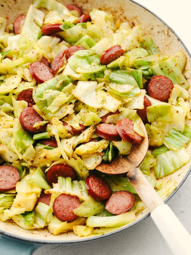 Sausage and cabbage is the easiest skillet recipe to throw together! In minutes, you'll have a tasty meal loaded with amazing meaty flavor and texture! Scooping sausage and cabbage with a wooden spoon.