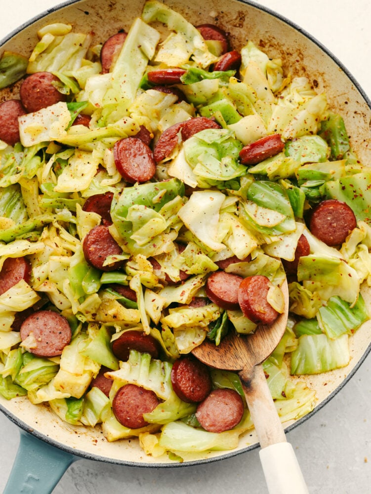Sausage and cabbage is the easiest skillet recipe to throw together! In minutes, you'll have a tasty meal loaded with amazing meaty flavor and texture! Cooked cabbage and sausage in a white skillet.