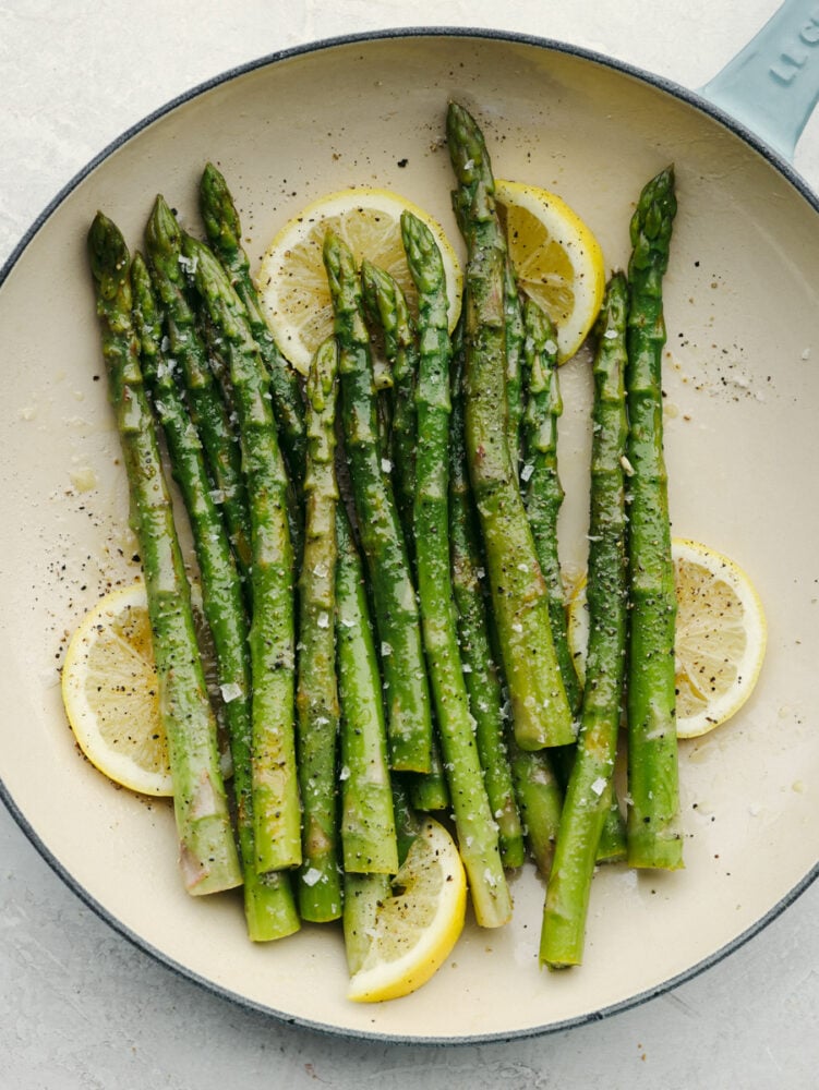 Steamed asparagus is the perfect addition to any meal! All it needs is a squeeze of lemon and freshly cracked salt and pepper to be a knockout side! Steamed asparagus, garnished with lemon, on a white and blue plate.