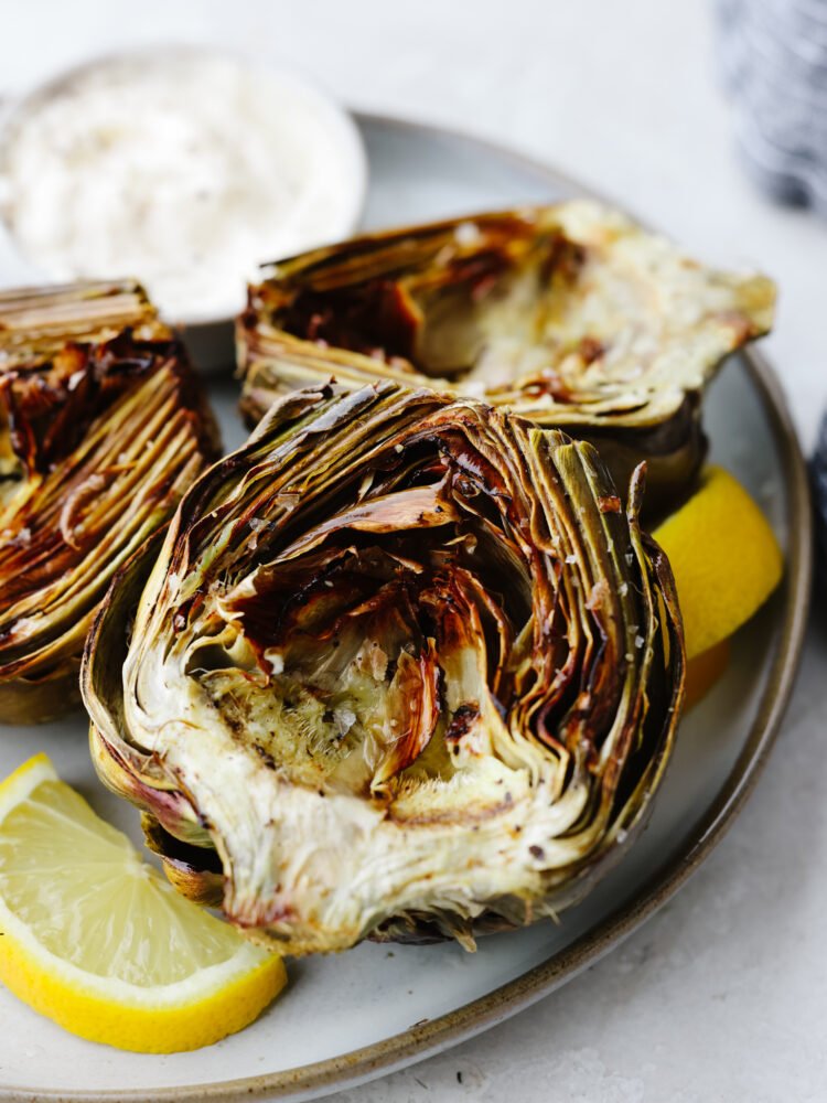 If you are looking for a simple and delicious way to cook up your artichokes that is quick and easy, then these air fryer artichokes are just for you! Cooked to perfection, these will be your new favorite vegetable! Cooked artichokes on a plate with lemon slices.