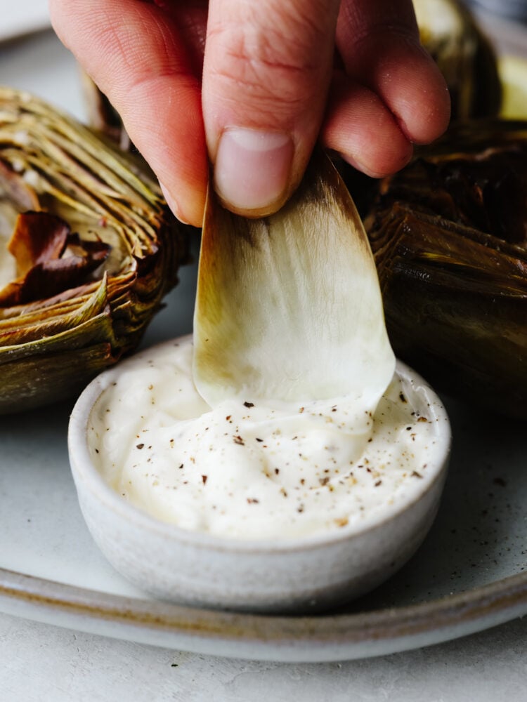 If you are looking for a simple and delicious way to cook up your artichokes that is quick and easy, then these air fryer artichokes are just for you! Cooked to perfection, these will be your new favorite vegetable! An artichoke leaf being dipped into some sauce.