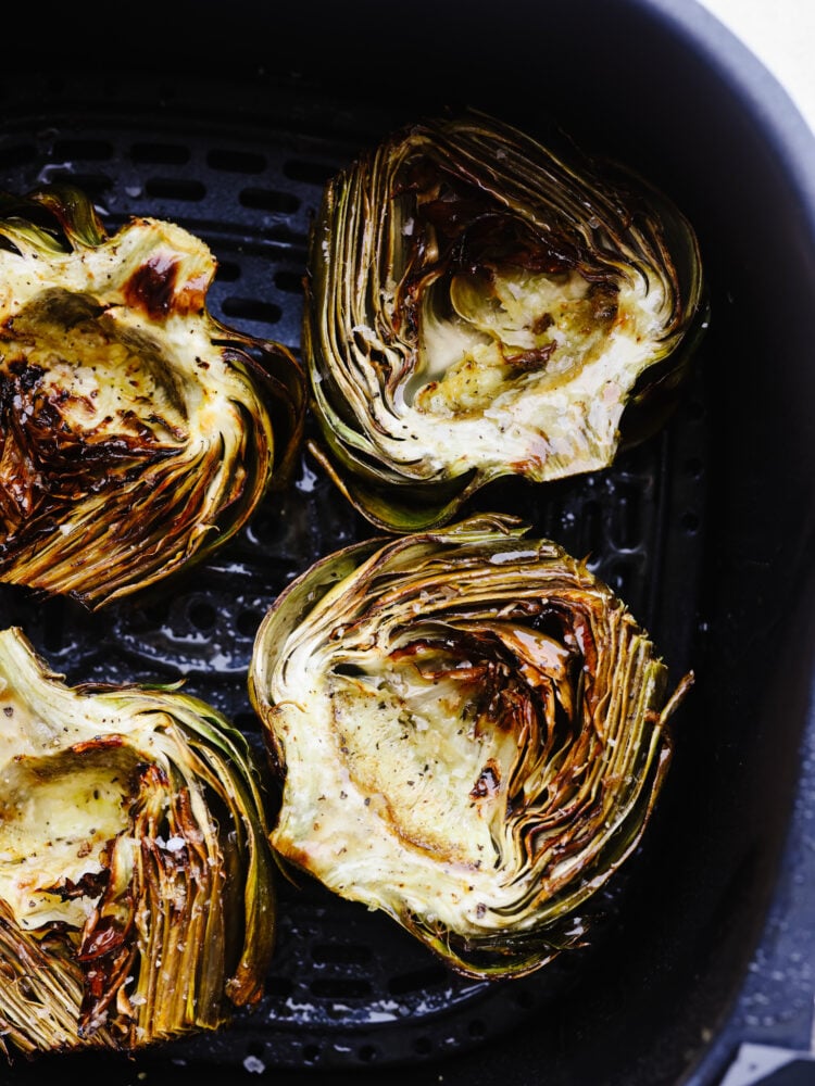 If you are looking for a simple and delicious way to cook up your artichokes that is quick and easy, then these air fryer artichokes are just for you! Cooked to perfection, these will be your new favorite vegetable! Artichokes cut in half in and air fryer basket.