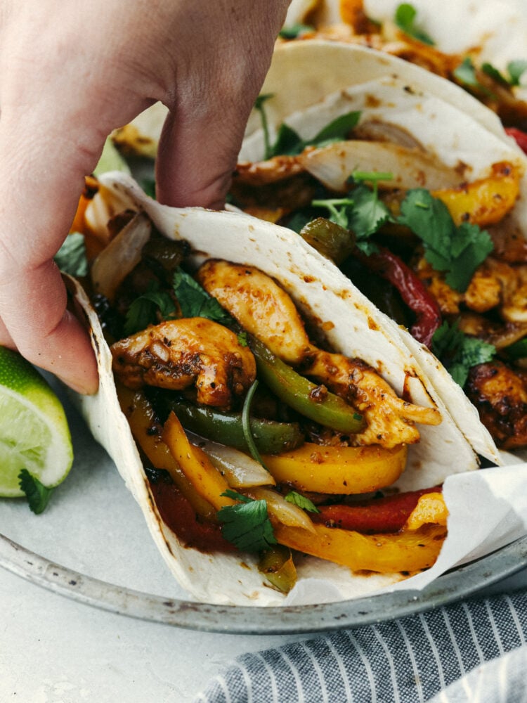 These air fryer fajitas are packed to the brim with flavor but only take a few minutes to make! They are perfect for those on-the-go, busy nights, and everyone will go crazy over them! A hand holding and air fryer chicken fajita in an small, flour tortilla.