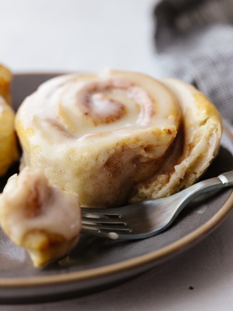 There is no easier way to cook cinnamon rolls out there! These air fryer cinnamon rolls from a can are so easy and delicious. They take less than 15 minutes to bake! A cinnamon roll on a plate with a silver fork cutting into it.