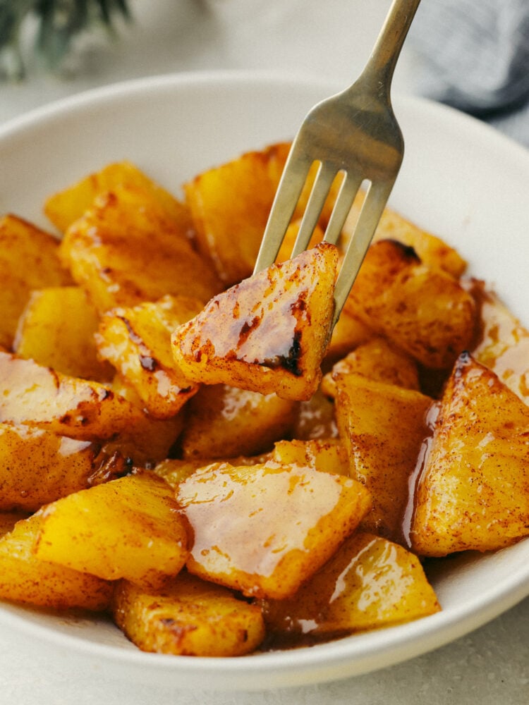 This amazing air fryer brown sugar pineapple is the easiest and most delicious snack! So juicy and sweet, this warm pineapple will become your new favorite way to eat this tropical fruit! Pineapple with brown sugar glaze in a bowl with a fork biting into a piece.