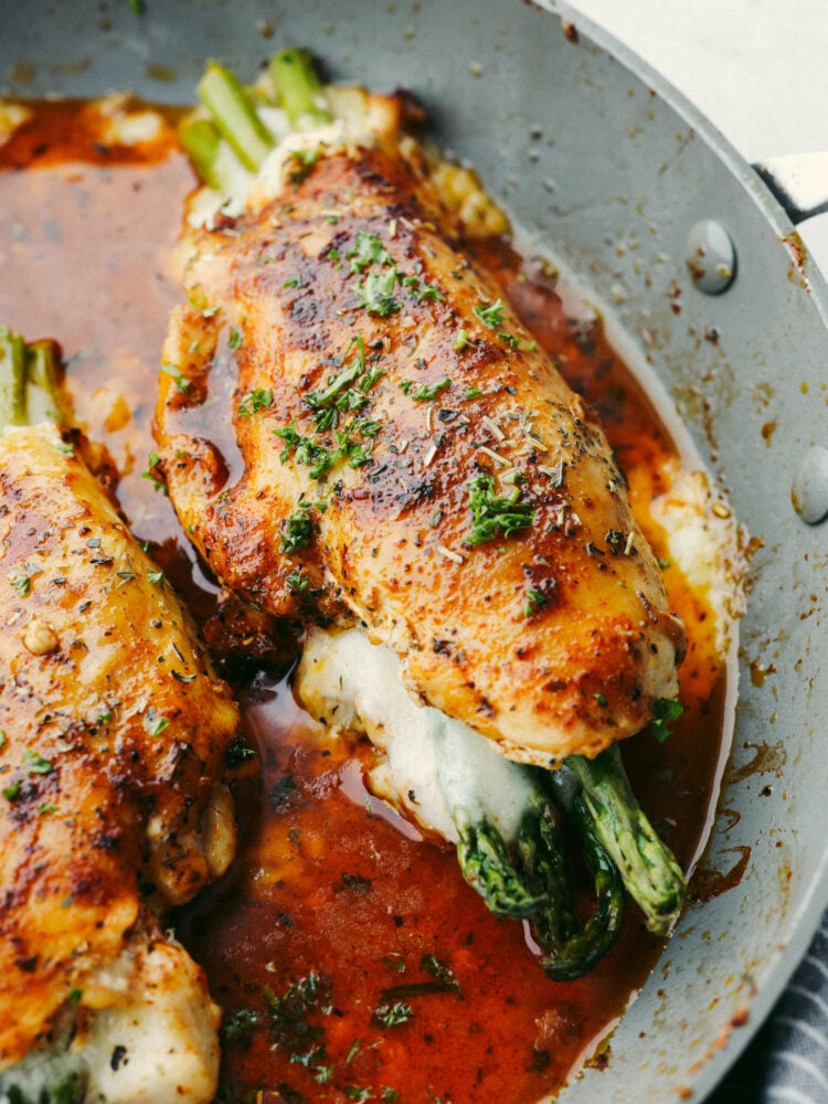 This asparagus stuffed chicken is incredibly juicy and tender. Flavored with the most delicious spices and stuffed with the incredibly healthy vegetable, asparagus, you will want to lick your plate clean! A close up of a pan with a chicken breast stuffed with cheese and asparagus.