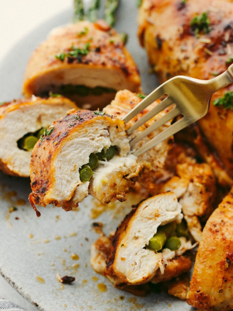 This asparagus stuffed chicken is incredibly juicy and tender. Flavored with the most delicious spices and stuffed with the incredibly healthy vegetable, asparagus, you will want to lick your plate clean! A chicken breast being cut into with a gold fork.