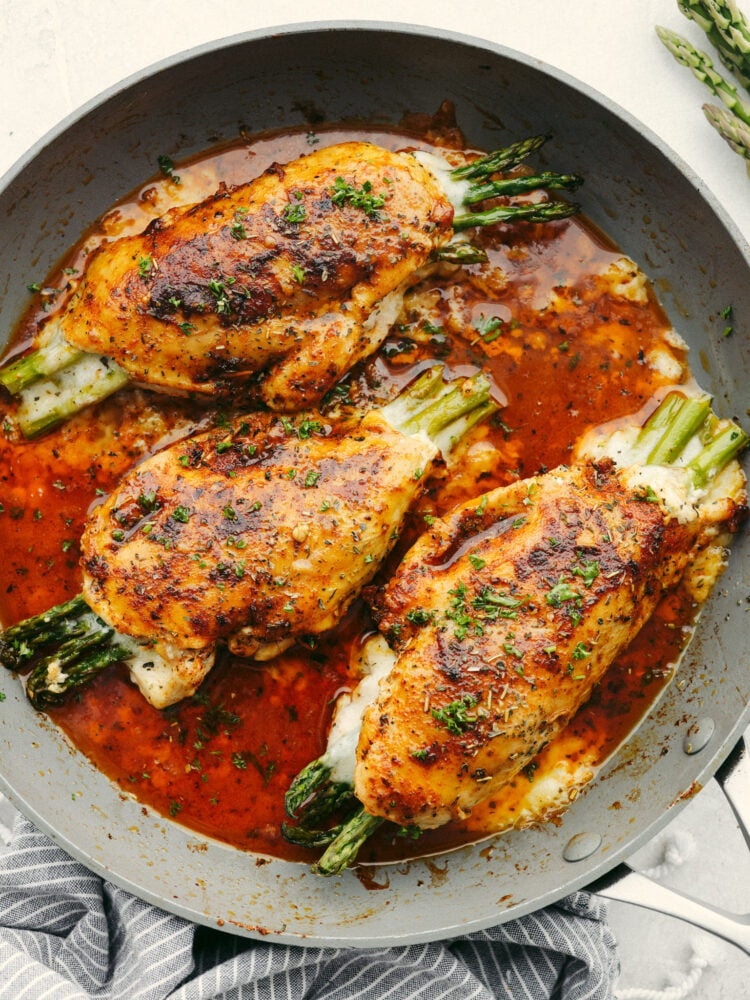 This asparagus stuffed chicken is incredibly juicy and tender. Flavored with the most delicious spices and stuffed with the incredibly healthy vegetable, asparagus, you will want to lick your plate clean! A pan nwith 3 asparagus stuffed chicken breasts.