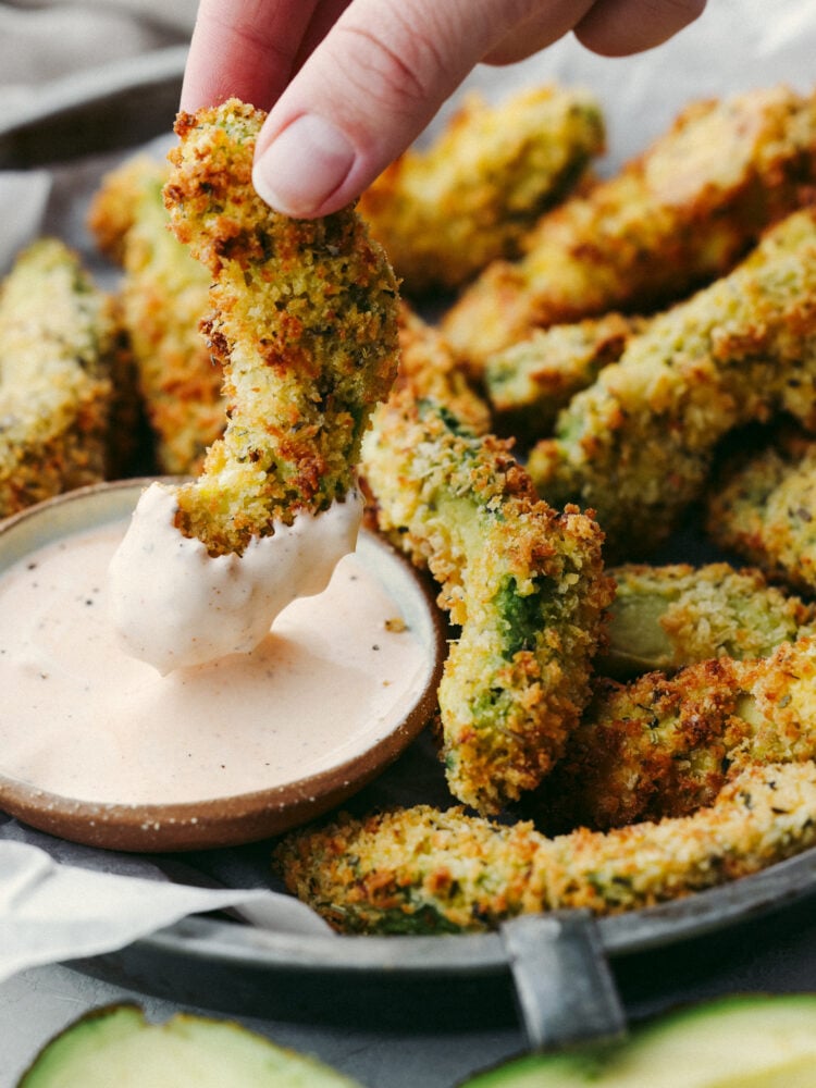 Crispy and creamy, air fryer avocado fries are a quick and easy snack that the whole family will love! They're so delicious and perfect for dipping! Closeup of dipping a slice of avocado in dip.