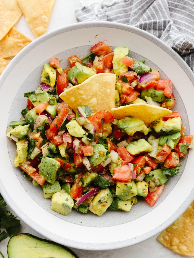 A bowl of avocado salsa with tortilla chips dipped in it.
