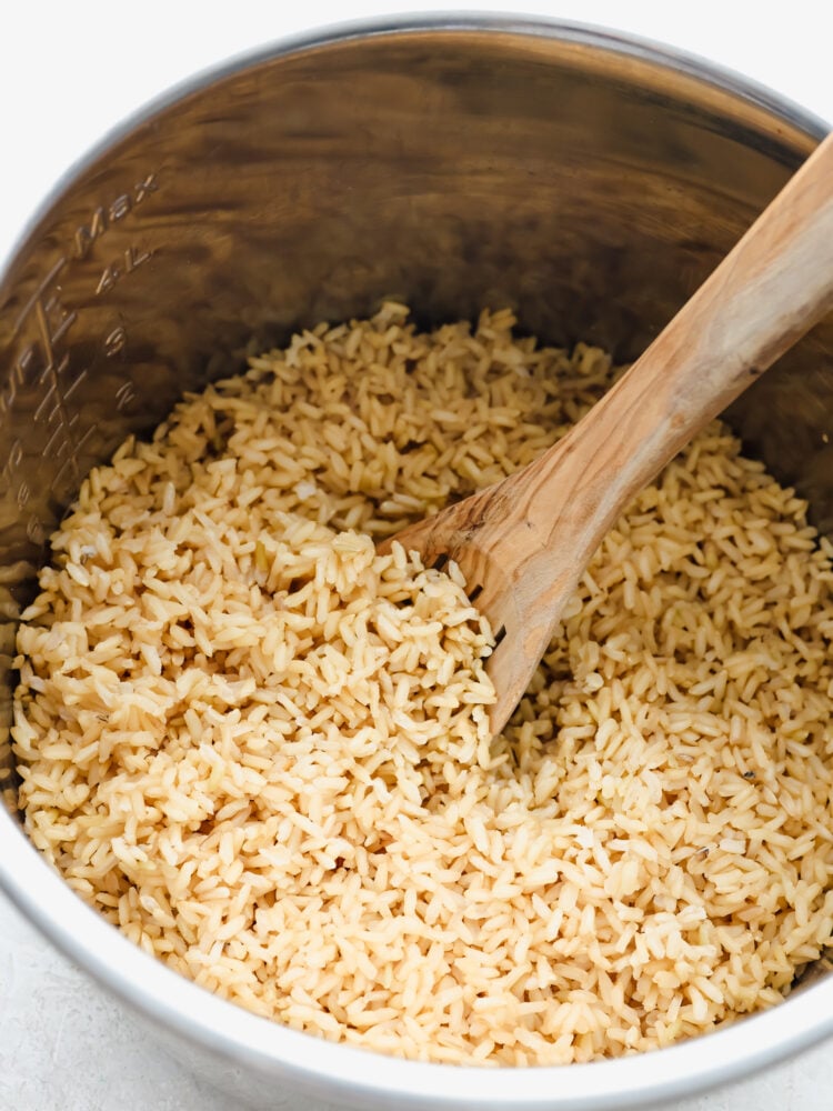 Brown rice can be tricky to get right. Make it in your Instant Pot and you'll have fresh, fluffy rice ready in 20 minutes! Hero image of brown rice in an Instant Pot, being stirred with a wooden spoon.